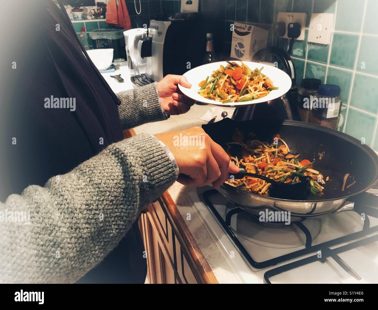 Woman in the kitchen, serving up a vegetarian stir fried supper Stock Photo