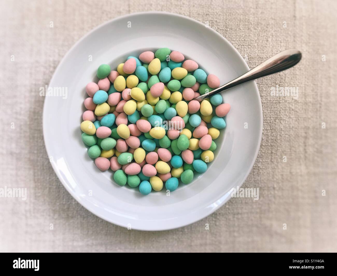 Bowl of colourful sugar-coated chocolate mini-eggs, with spoon. A fun but not-so-healthy Easter breakfast. - Smartphone Captured Stock Image