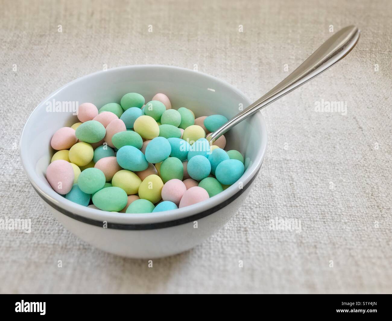 Bowl full of colourful sugar-coated chocolate mini-eggs, with spoon sticking out. - Smartphone Captured Stock Image