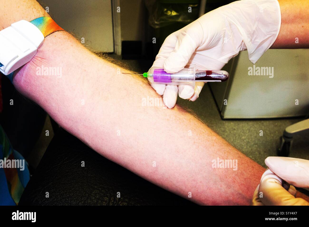 A practice nurse takes a blood sample from the arm of a middle aged man as part of an NHS health check test. Uk - Smartphone Captured Stock Image