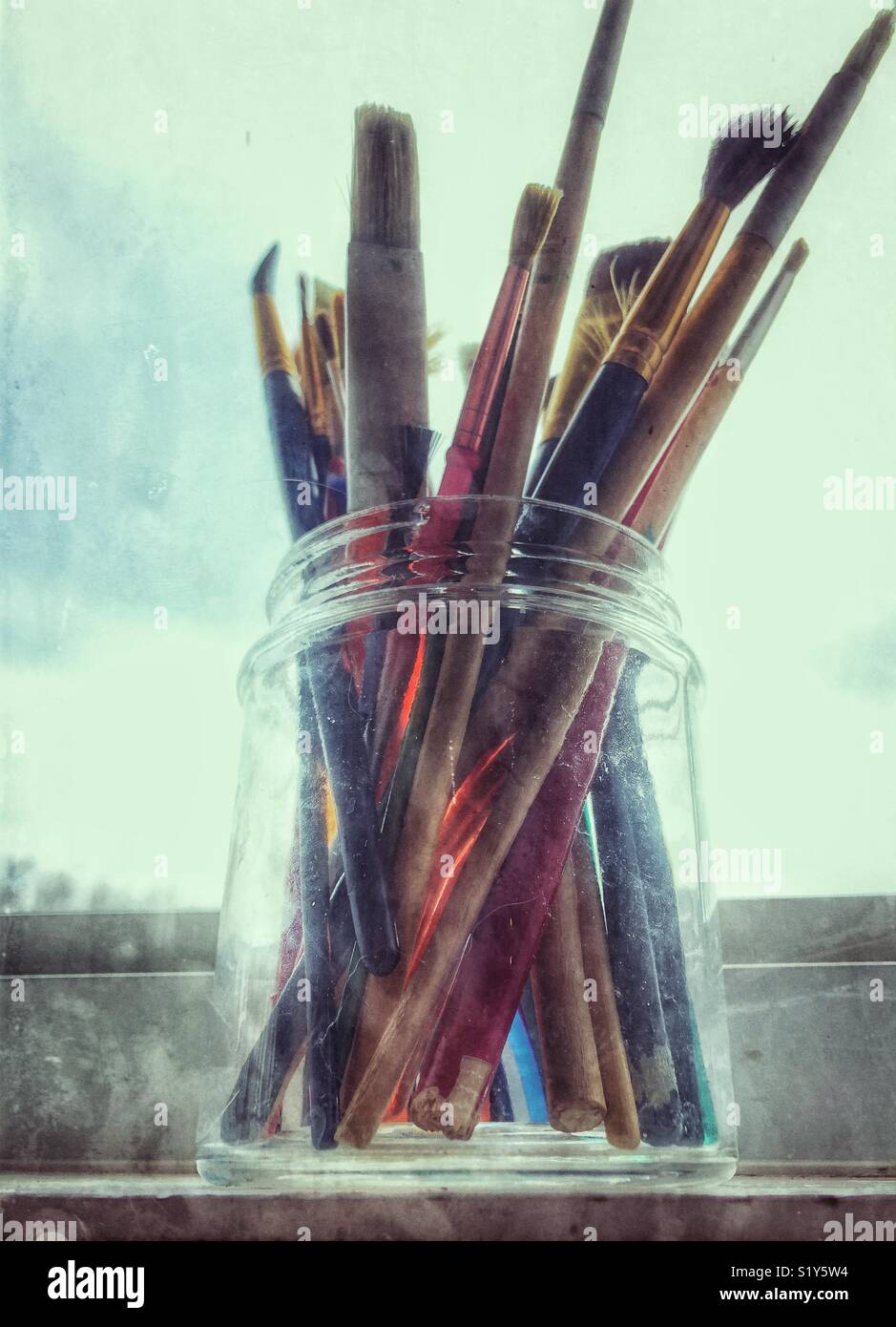 Mixed paint brushes in glass jar on windowsill - Smartphone Captured Stock Image