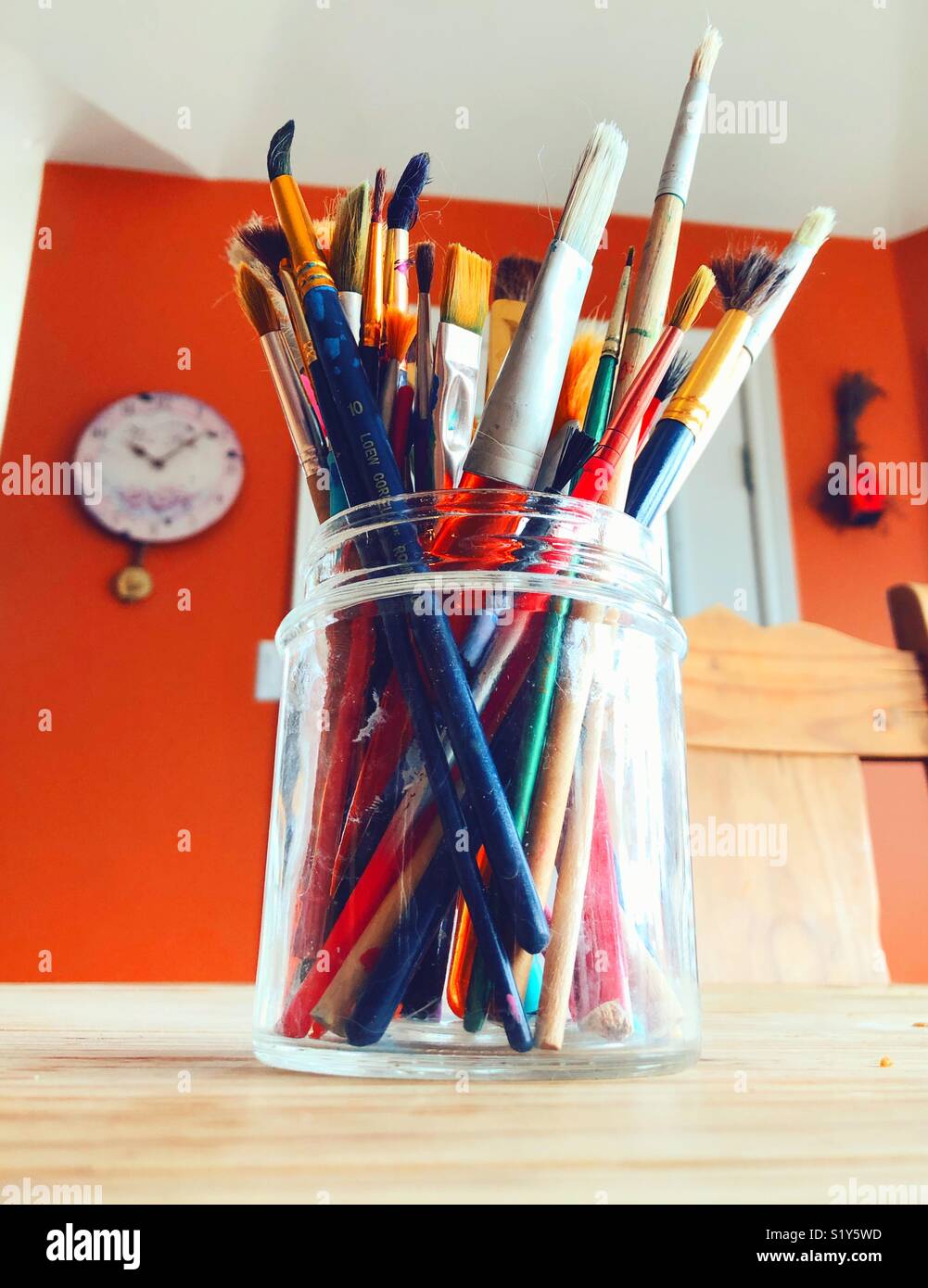 Brightly coloured mixed paintbrushes in a glass jar on a wooden table Stock Photo