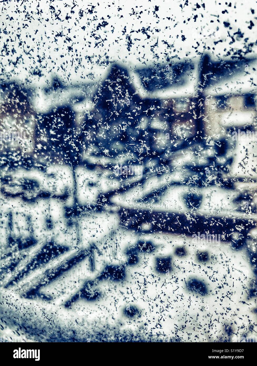Abstract view through a window covered in ice and snowflakes looking down to houses in a residential courtyard during Storm Emma, March 2018 - Smartphone Captured Stock Image