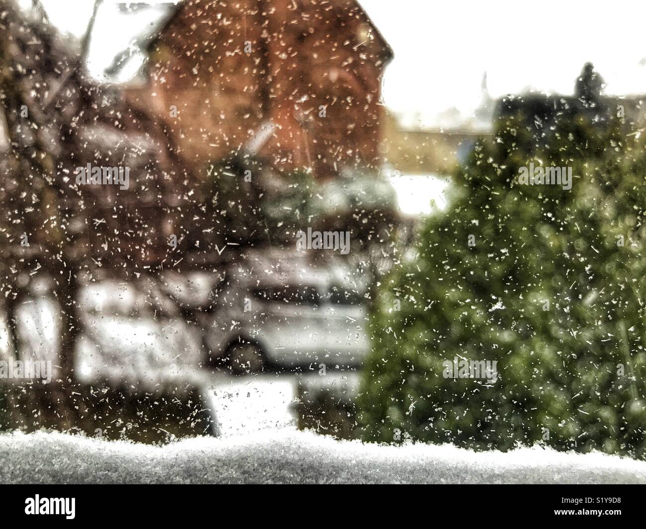 Abstract view looking out of a window covered in ice and snowflakes with snow piling up, down to car parked outside house, during Storm Emma, March 2018 - Smartphone Captured Stock Image