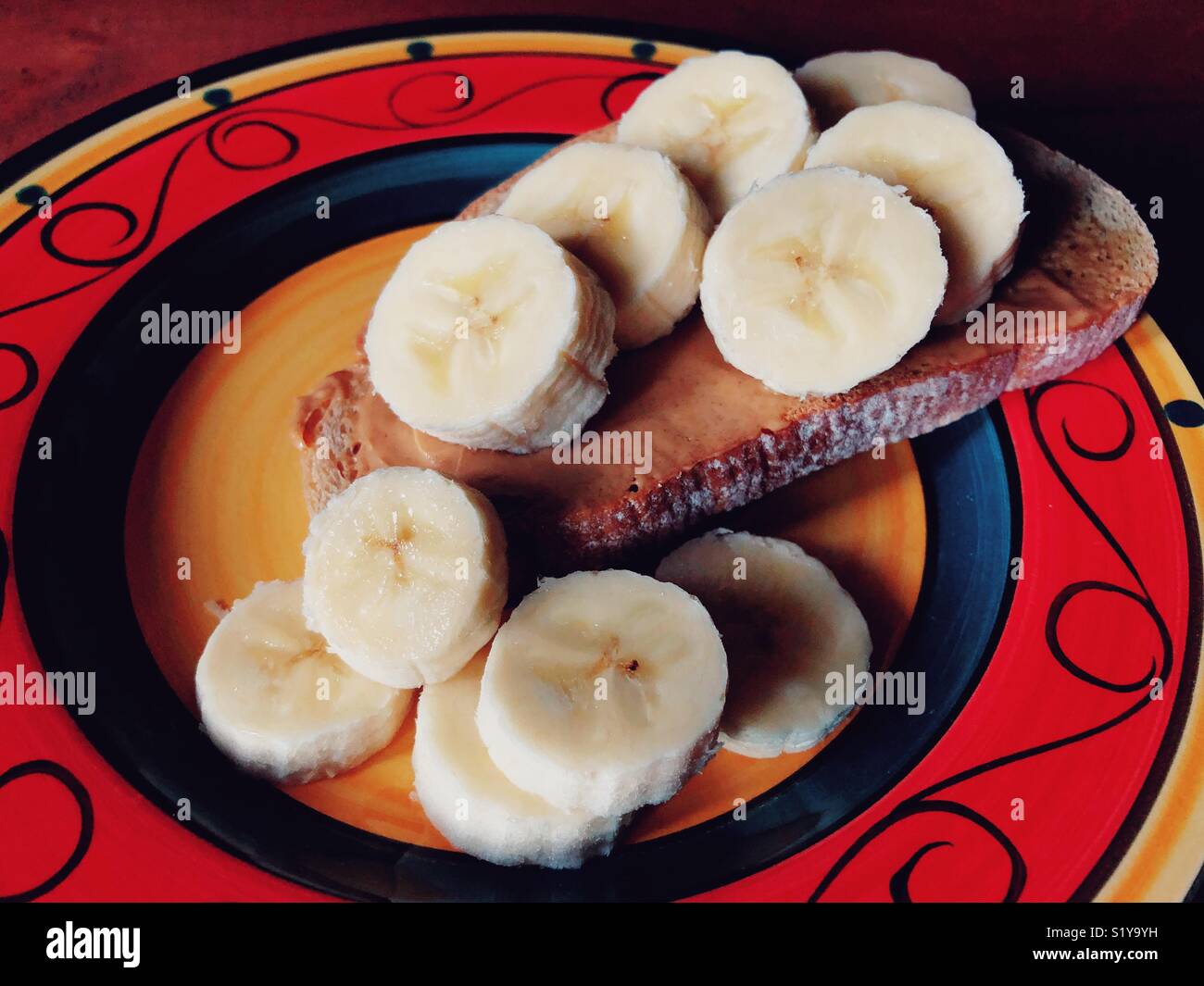 Closeup of peanut butter and banana slices on one piece of rye toast on a colourful plate - Smartphone Captured Stock Image