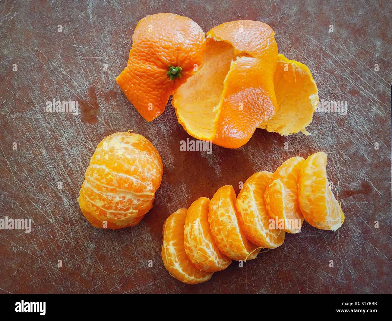 Freshly peeled clementine orange on cutting board showing pieces, half, and peel - Smartphone Captured Stock Image