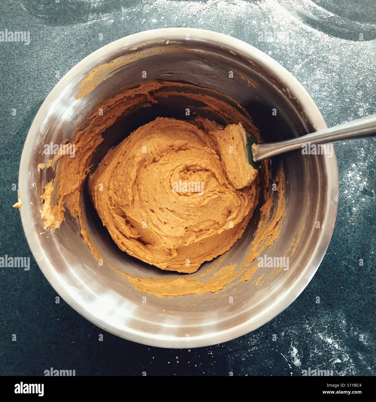 Stainless steel bowl full of pumpkin cookie batter with spatula and flour covered counter surface in background - Smartphone Captured Stock Image
