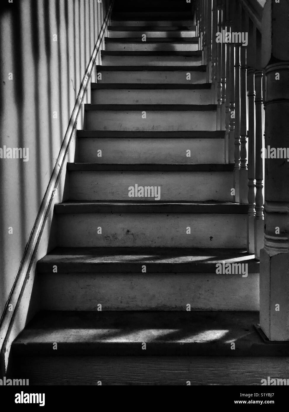 Black and white image looking up a dirty staircase with spindle shadows - Smartphone Captured Stock Image