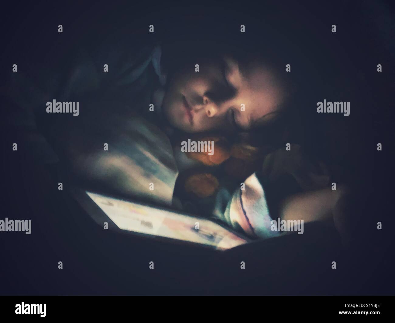 Child sleeping in the dark with tablet illuminating face - Smartphone Captured Stock Image