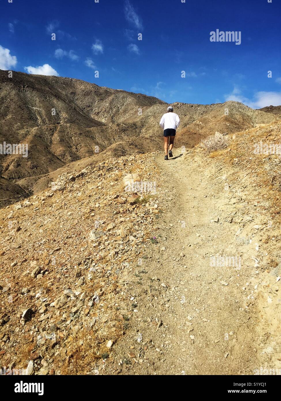 Man in his 60s jogging on the steep mountainous Bump and Grind trail in Palm Desert, Southern California USA - Smartphone Captured Stock Image