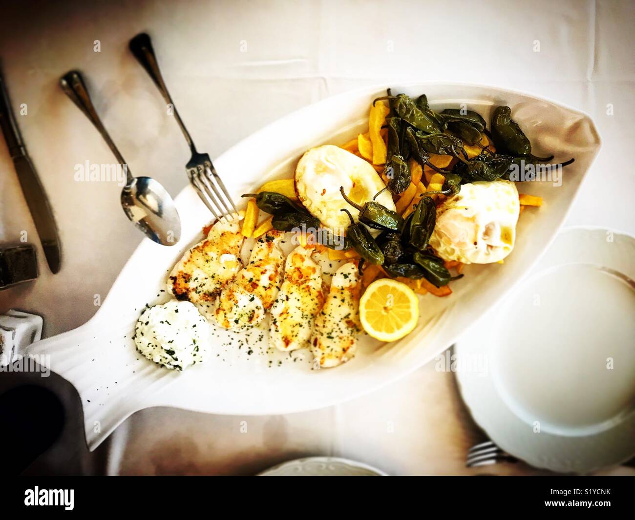 A plate with the shape of a fish with fish, fried eggs, fried peppers and potatoes in a restaurant in Andalusia, Spain - Smartphone Captured Stock Image