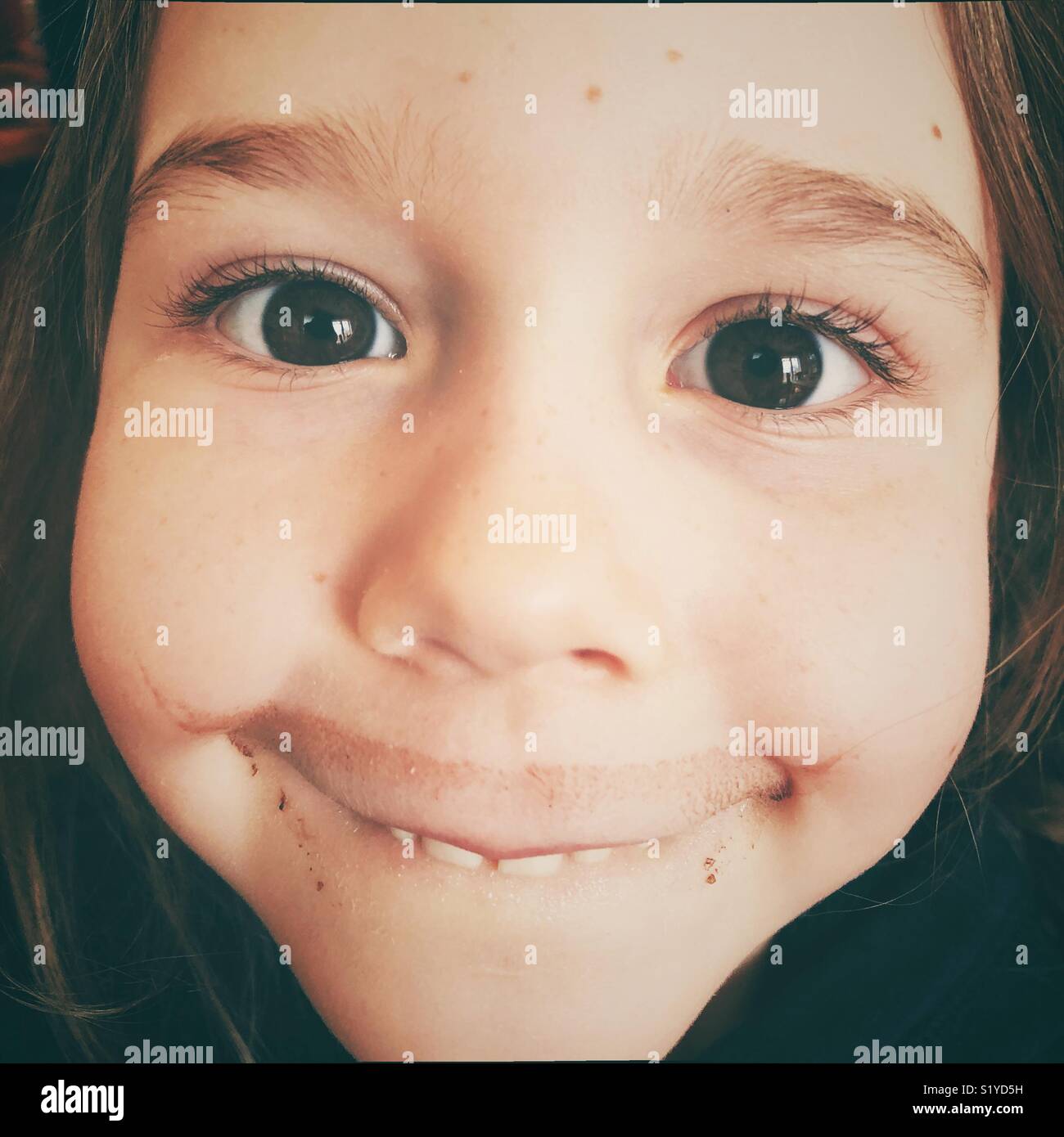 Closeup portrait of young brown eyed girl looking at camera with chocolate milk moustache and silly smile Stock Photo