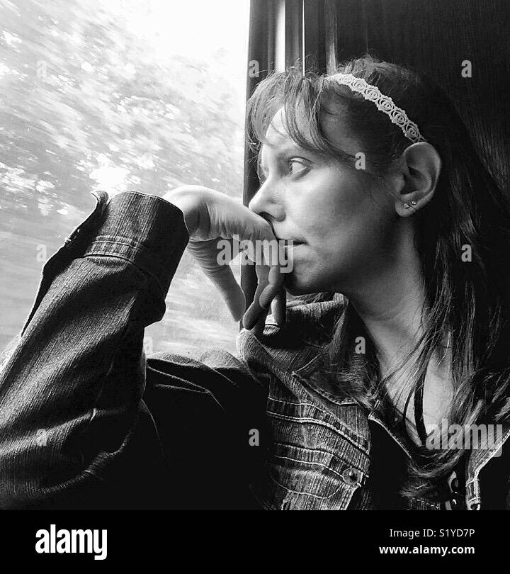 A woman watches out a window while riding a train. - Smartphone Captured Stock Image