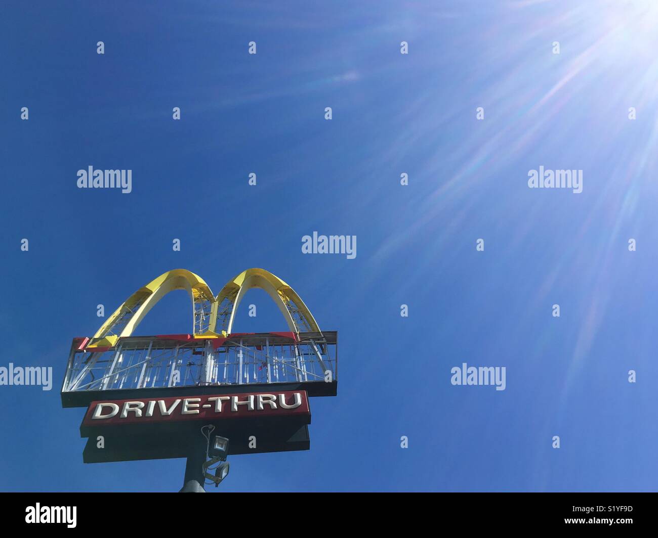 A derelict Mc Donald’s drive through sign against a clear blue sky and sun flare. - Smartphone Captured Stock Image
