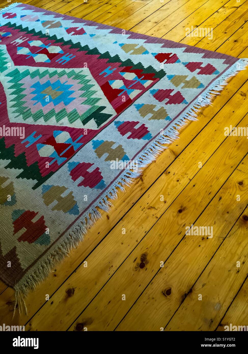 Flat-weave oriental rug on gleaming pine floor - Smartphone Captured Stock Image