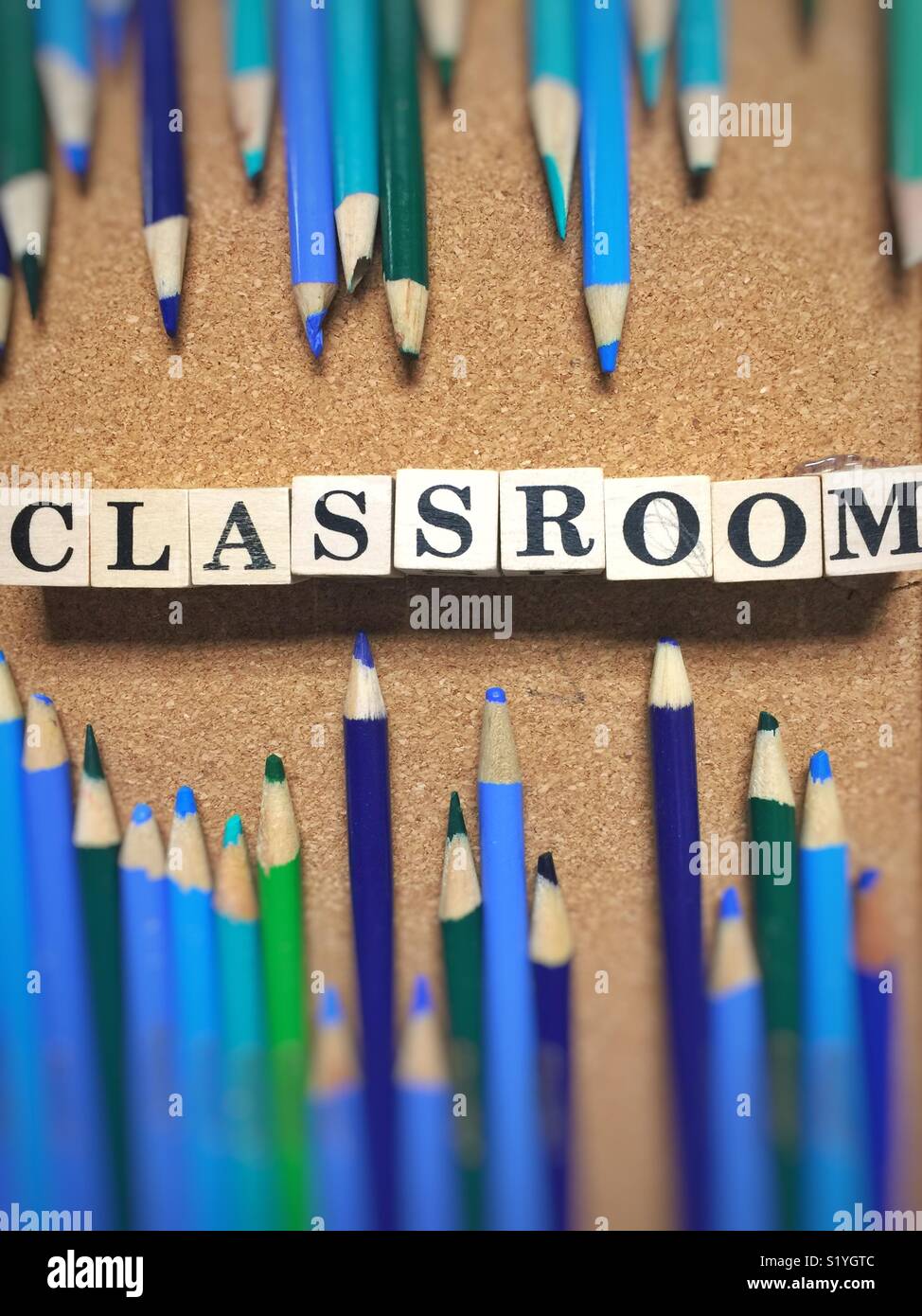 Word Classroom made with blocks surrounded by blue and green colored pencils on cork board Stock Photo