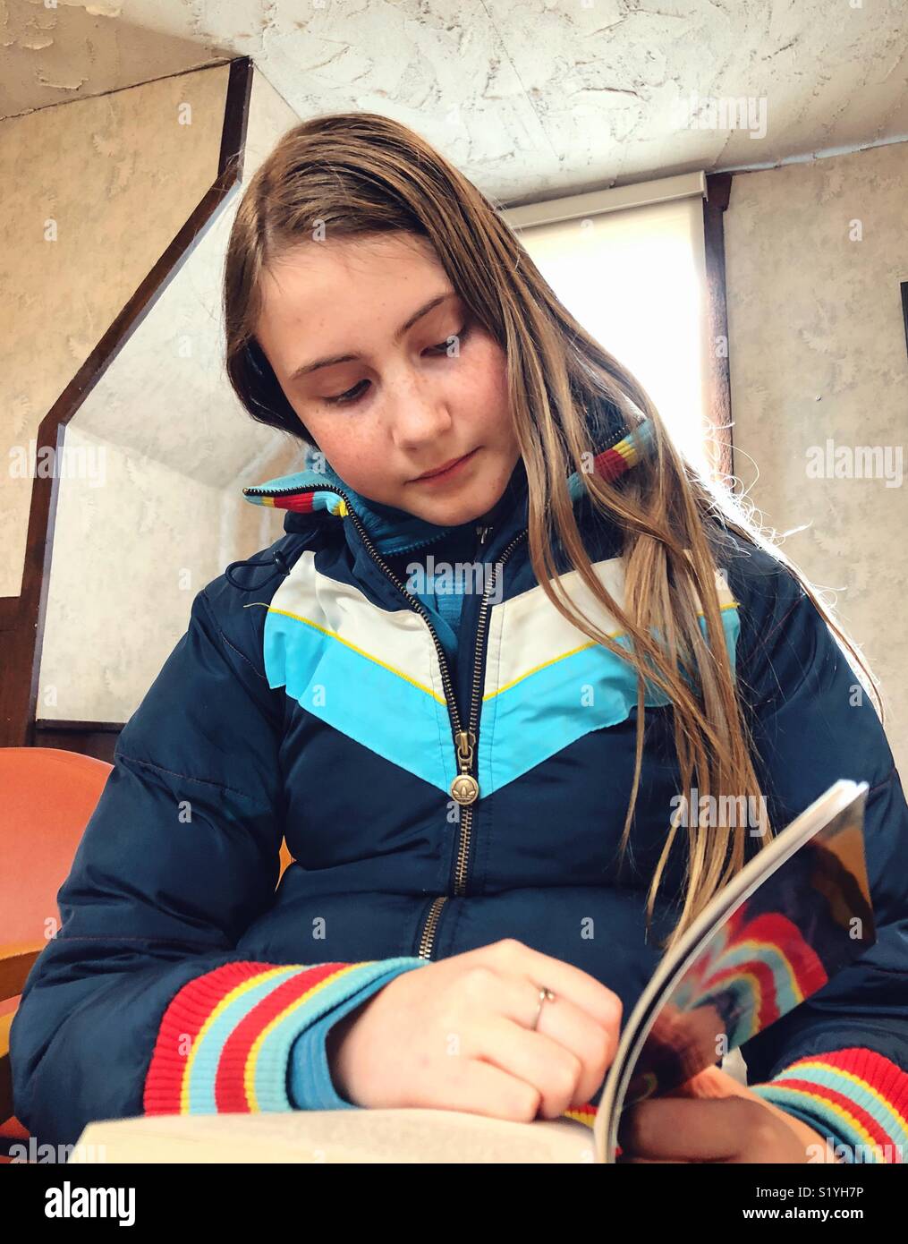 12 year old girl sitting in a library reading a novel - Smartphone Captured Stock Image
