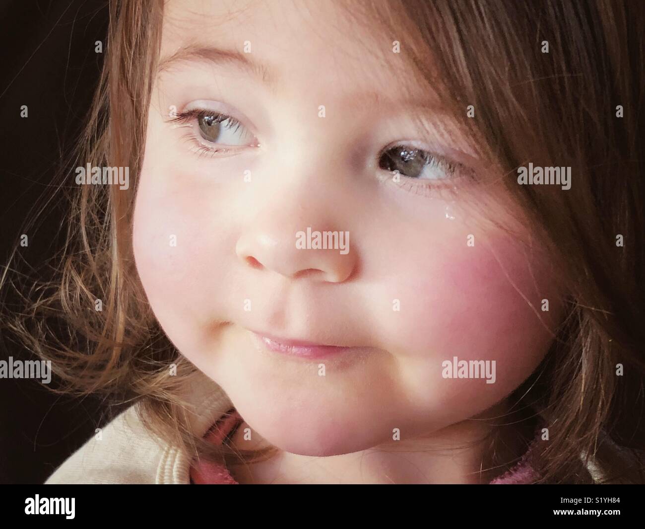 Closeup portrait of 2 year old girl looking to the side with single tear below one eye Stock Photo