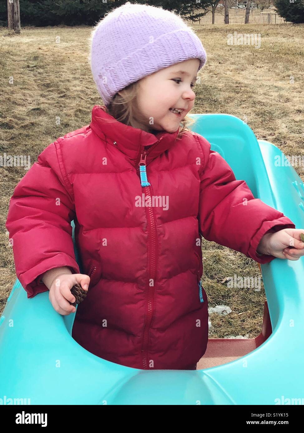 Toddler girl on plastic play structure in backyard/garden smiling looking to the side Stock Photo
