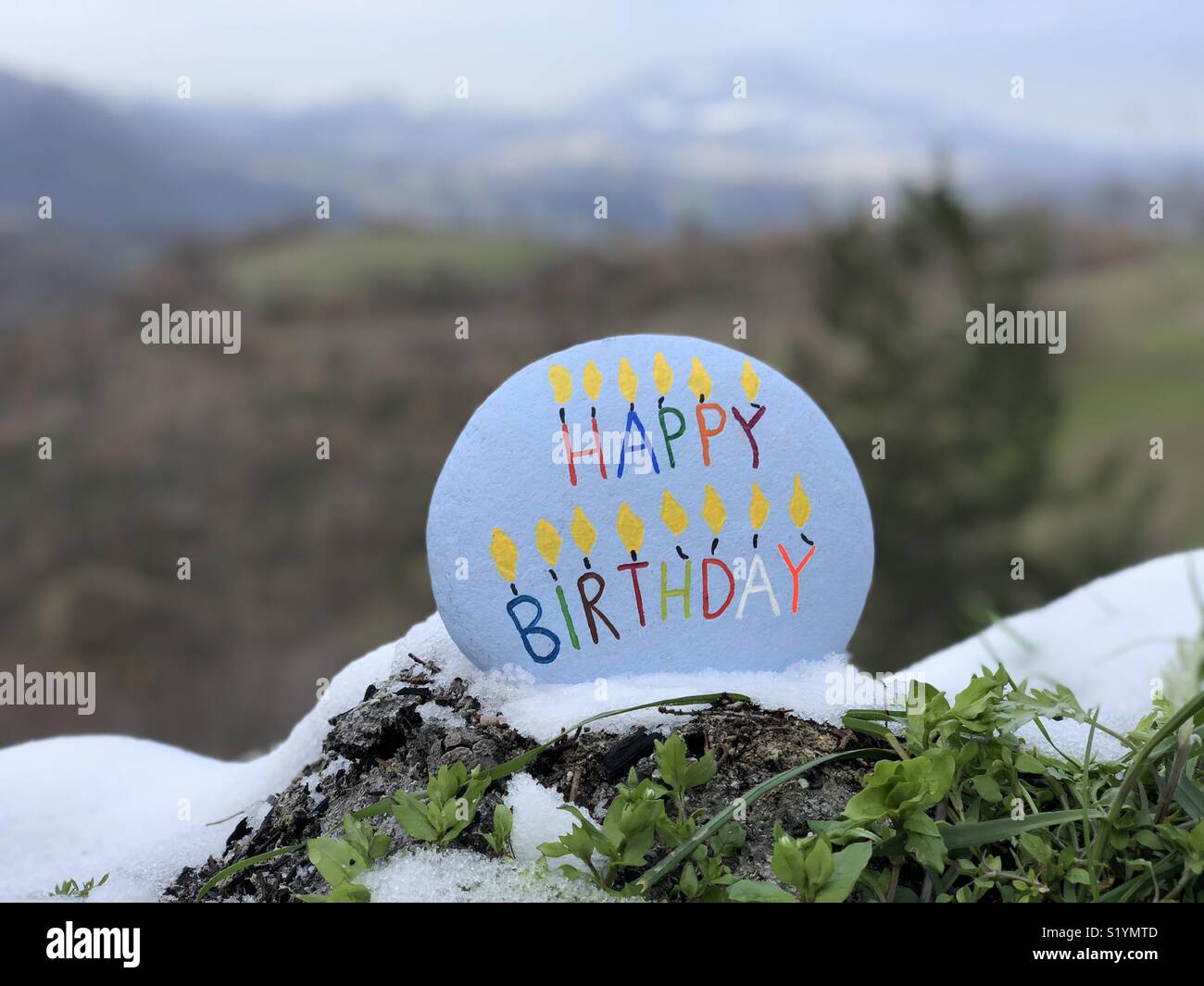 Happy Birthday text carved and colored on a stone with mountains background Stock Photo