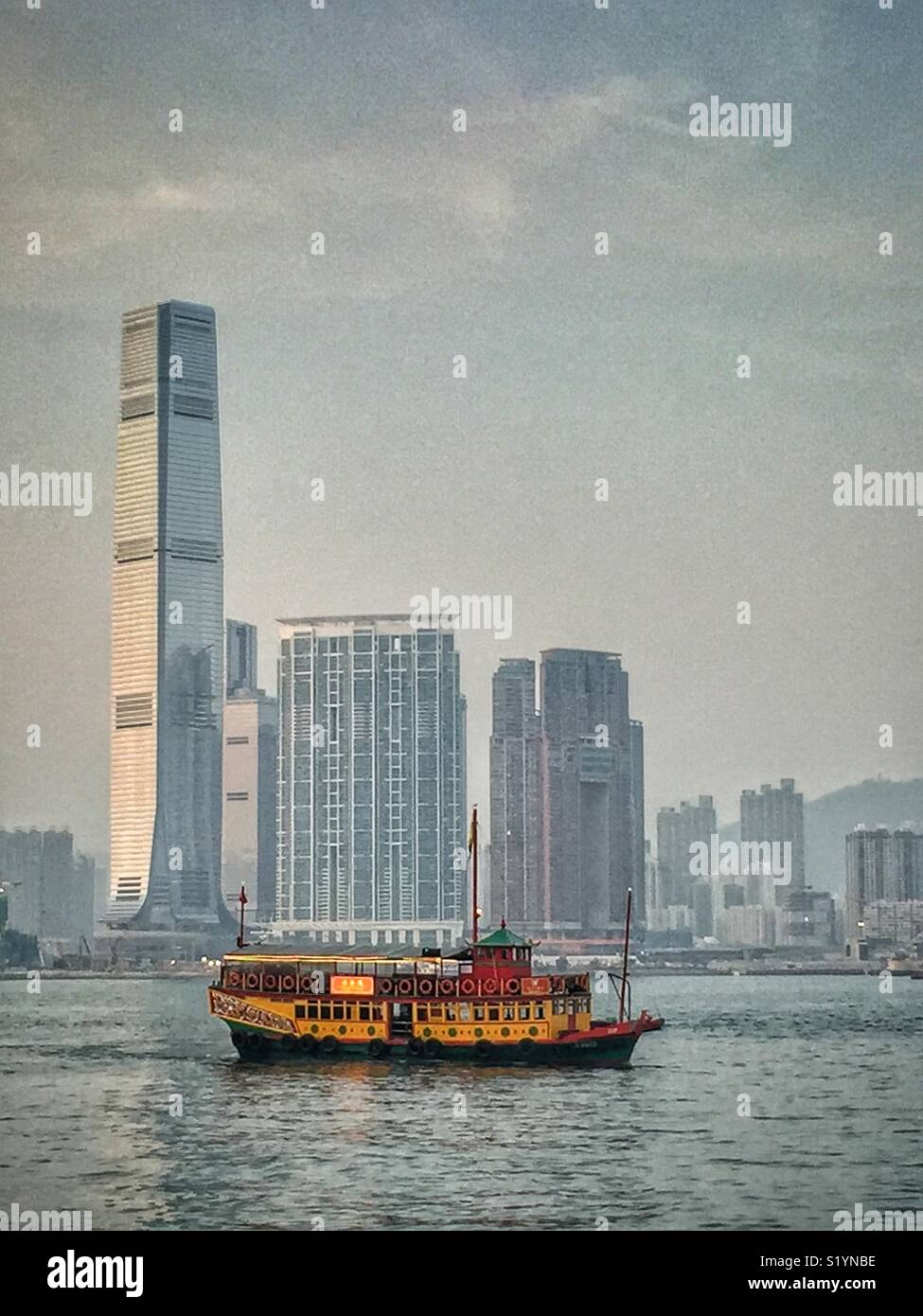The ‘Wing On Travel’, a double decker Chinese junk, carrying tourists on a sightseeing cruise on Victoria Harbour at twilight, in front of the ICC, Hong Kong’s tallest skyscraper, in West Kowloon - Smartphone Captured Stock Image
