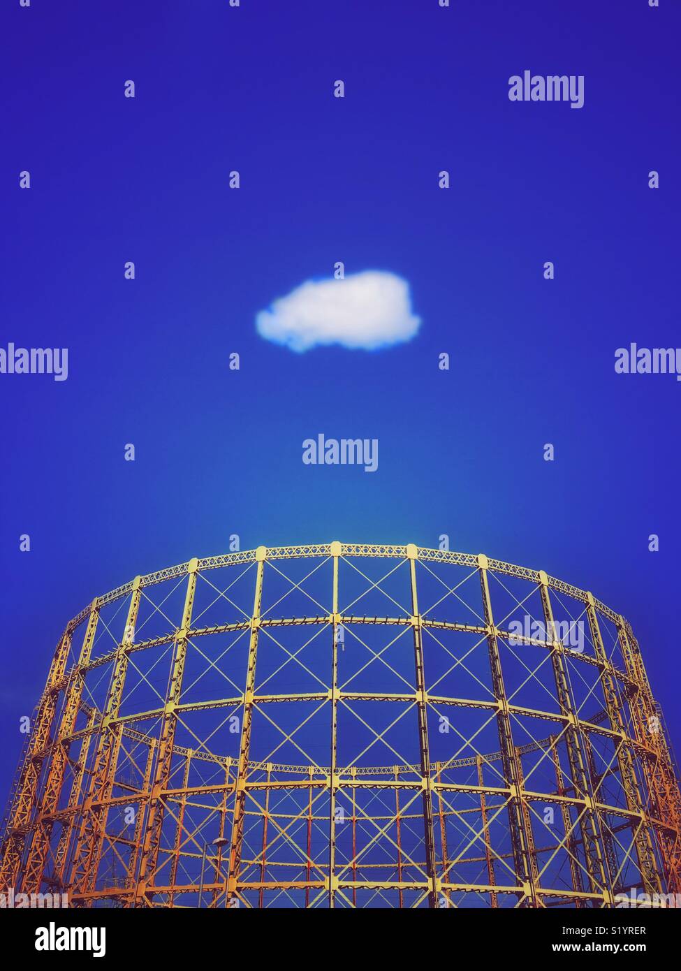 Gasometer structure against a vivid blue sky with solitary white cloud Stock Photo