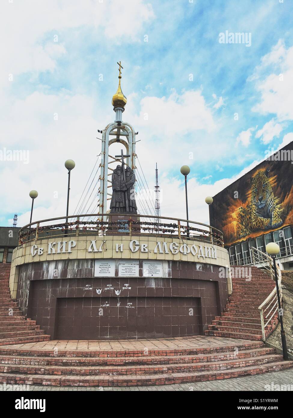 View point in Vladivostok, Russia. Collapsing sign and monument to Saints Cyril and Methodius and mural with Amur leopard on a wall. - Smartphone Captured Stock Image