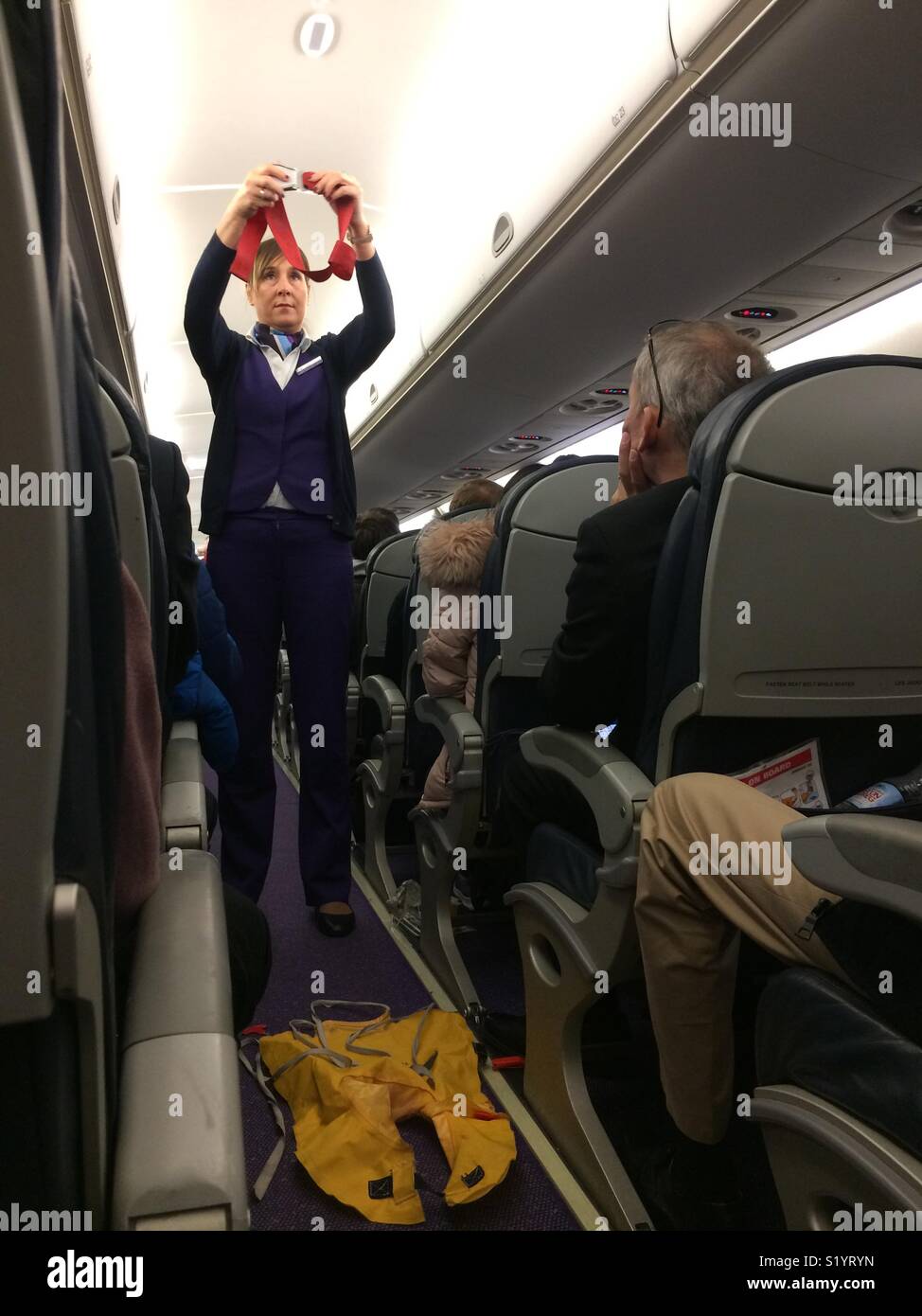 Cabin crew member giving the obligatory pre- flight safety demonstration on a Flybe Embraer 195 aircraft. She hold up a lap belt to demonstrate how it is fastened and unfastened. Stock Photo