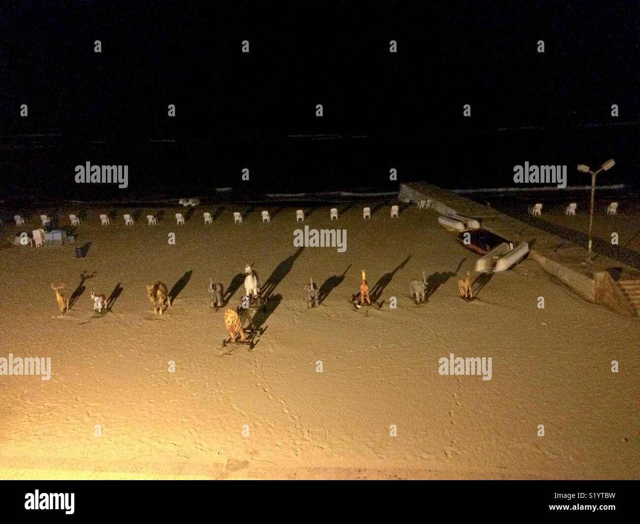 Zoo animals swing in front of chairs beyond boats on Alexandria seashore. - Smartphone Captured Stock Image