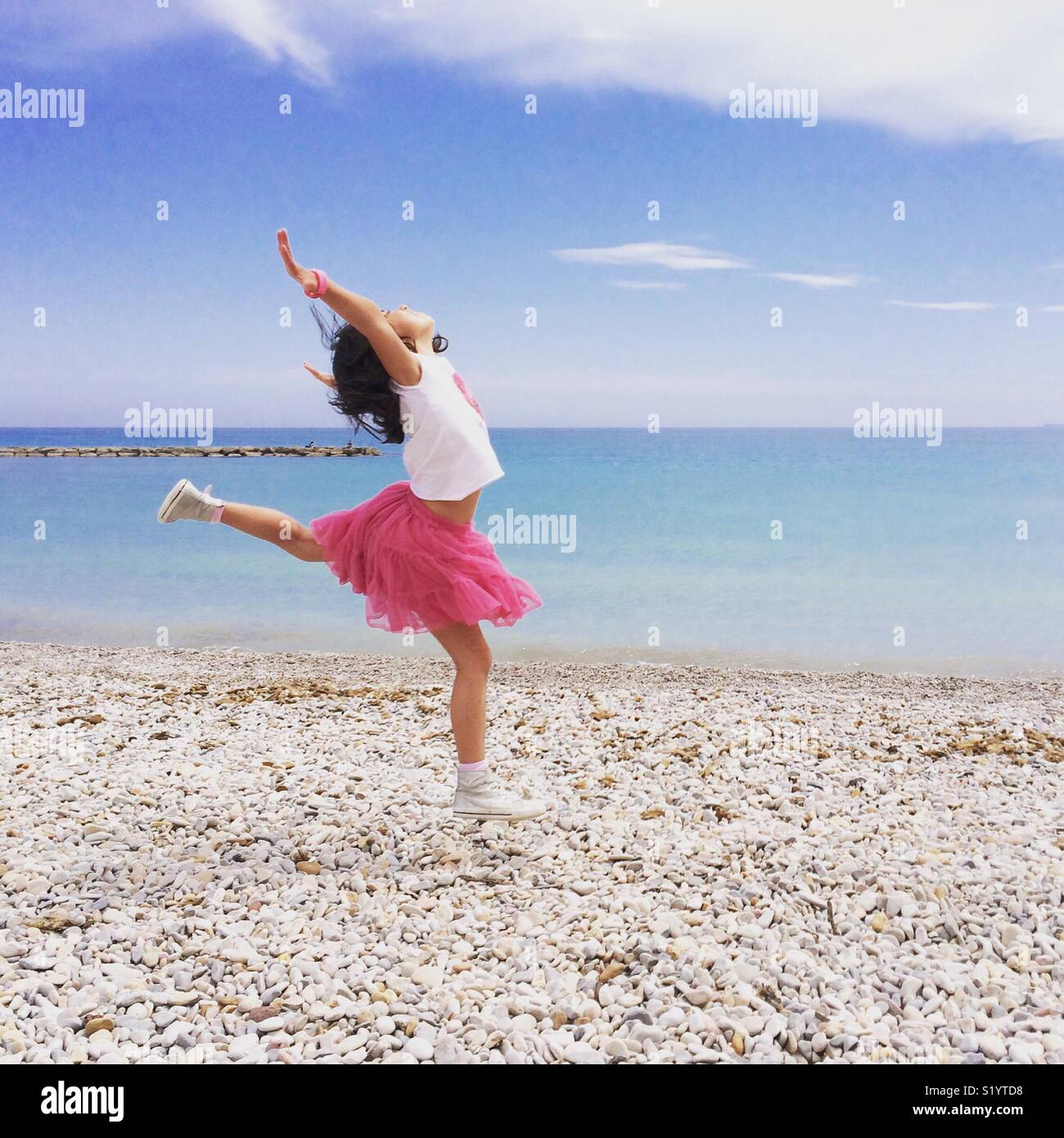 Girl in pink skirt dancing by the shore of the Mediterranean Sea Stock Photo