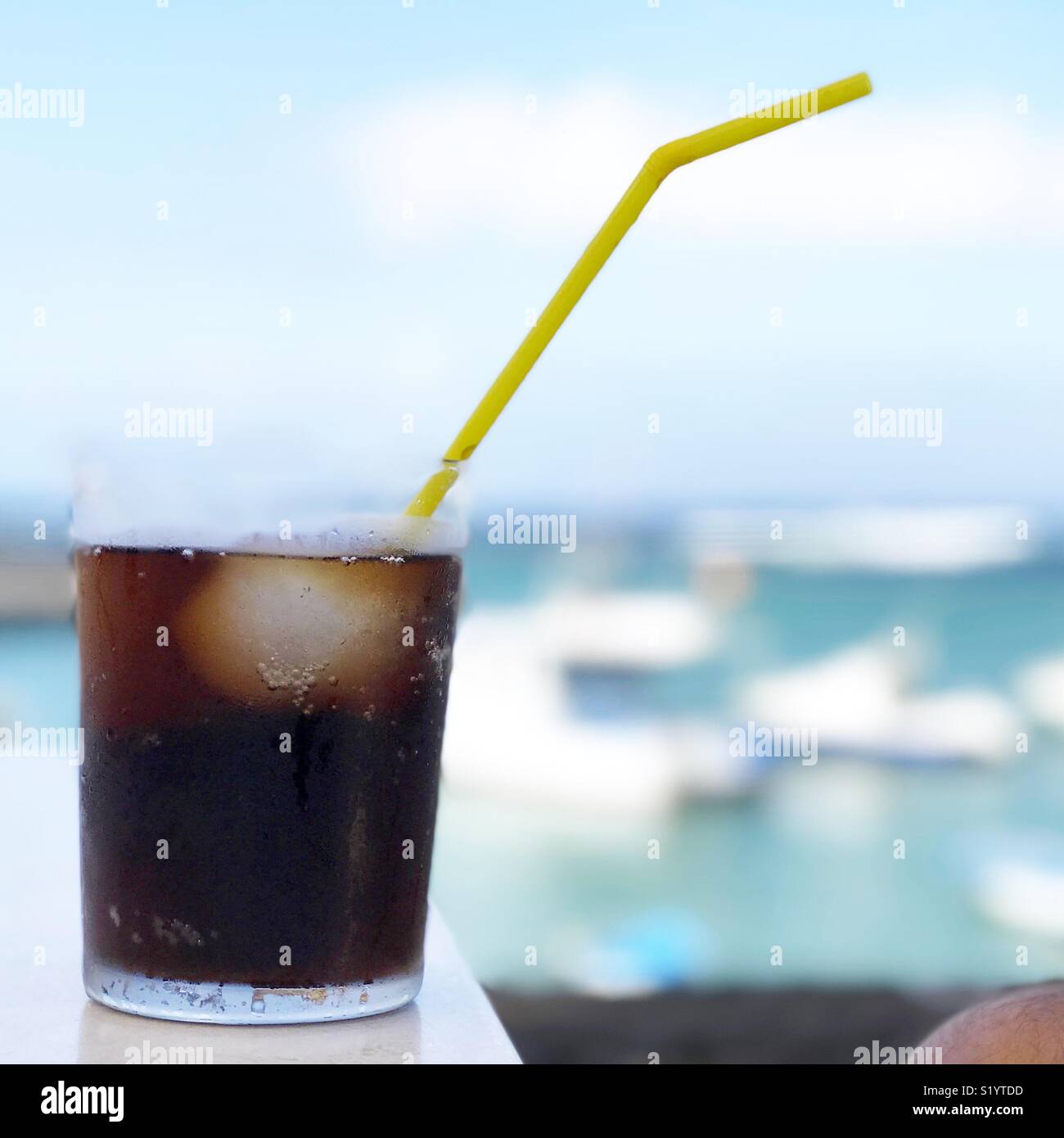 Glass of soda with a yellow straw by the marina Stock Photo