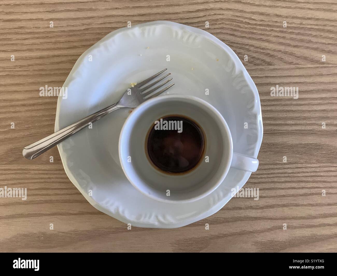 Empty plate and cup of coffee and a fork over a wood table - Smartphone Captured Stock Image