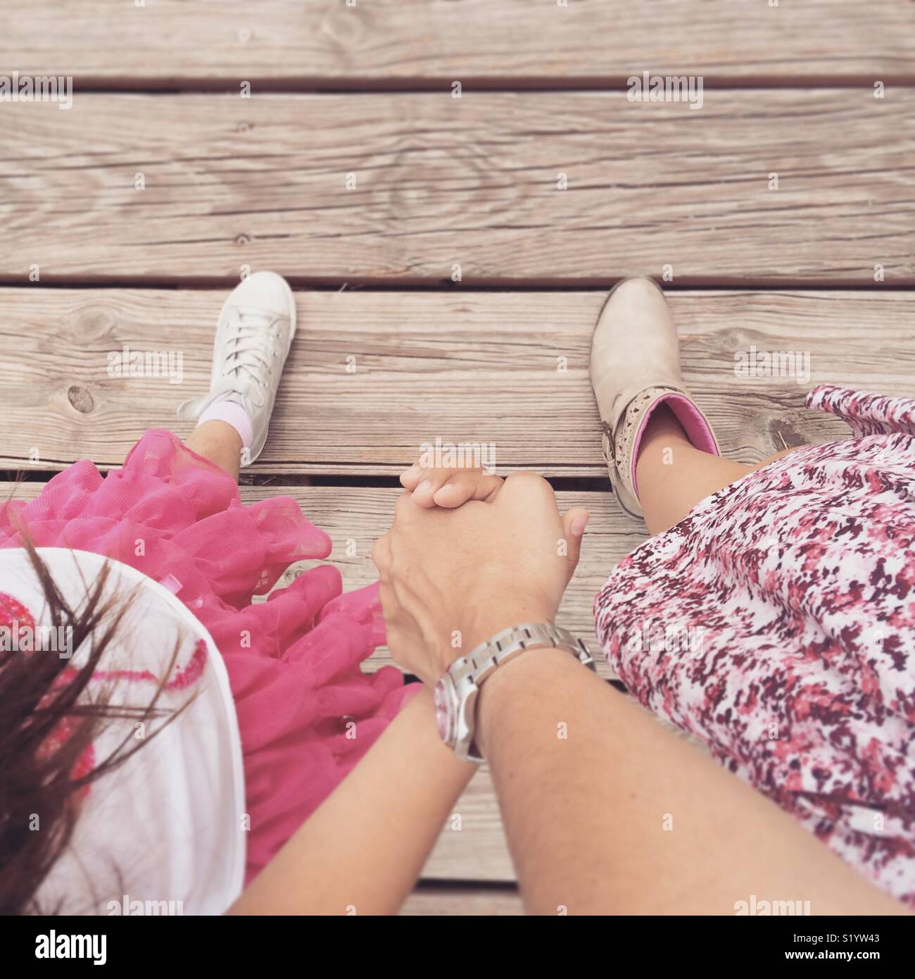 Mother and daughter in pink skirts walking hand by hand on a wood floor - Smartphone Captured Stock Image