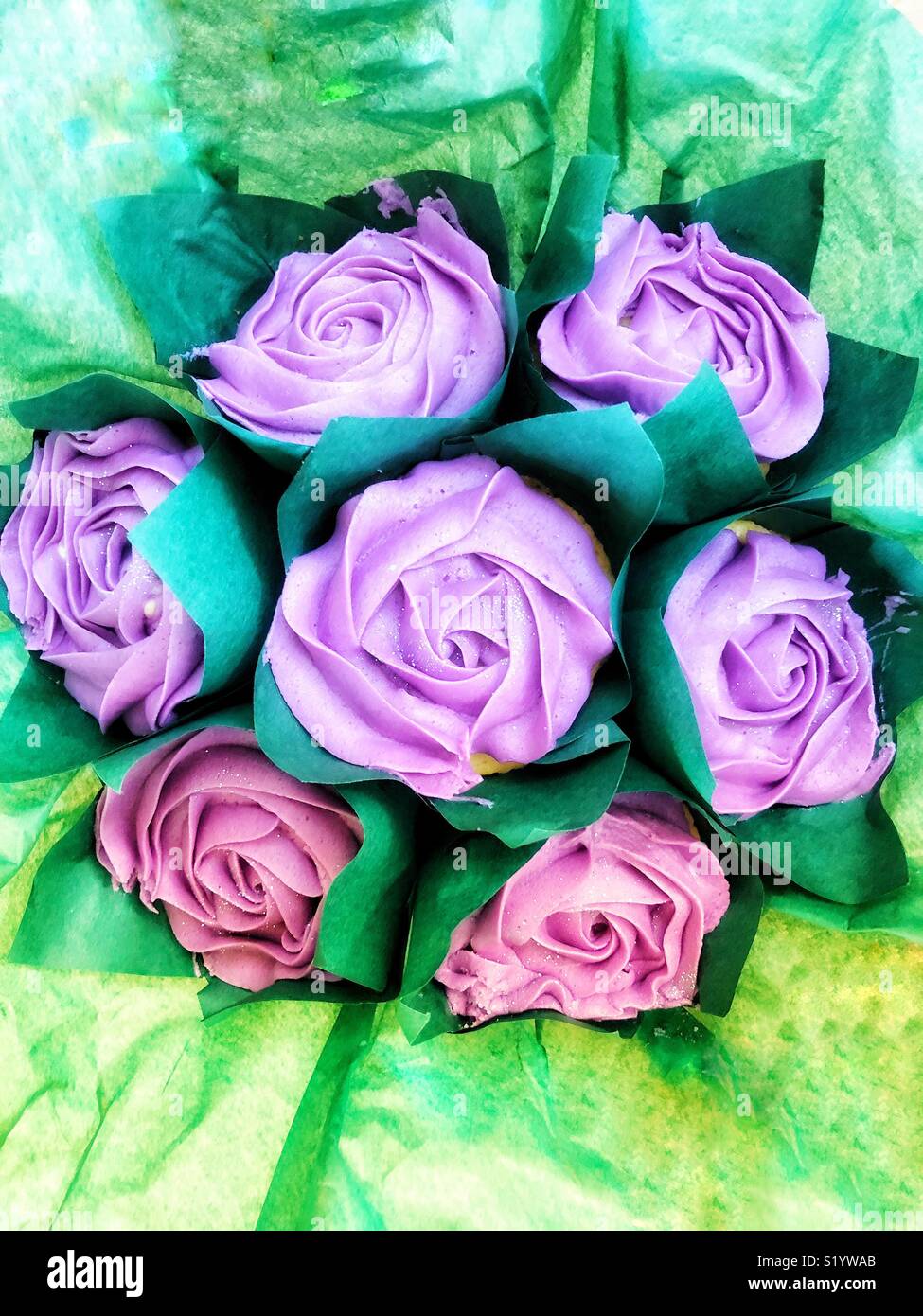 Bouquet of seven edible flowers, piped icing flowers on top of cup cakes with green grease proof paper for leaves. Food art realistically representing a bouquet of flowers. - Smartphone Captured Stock Image