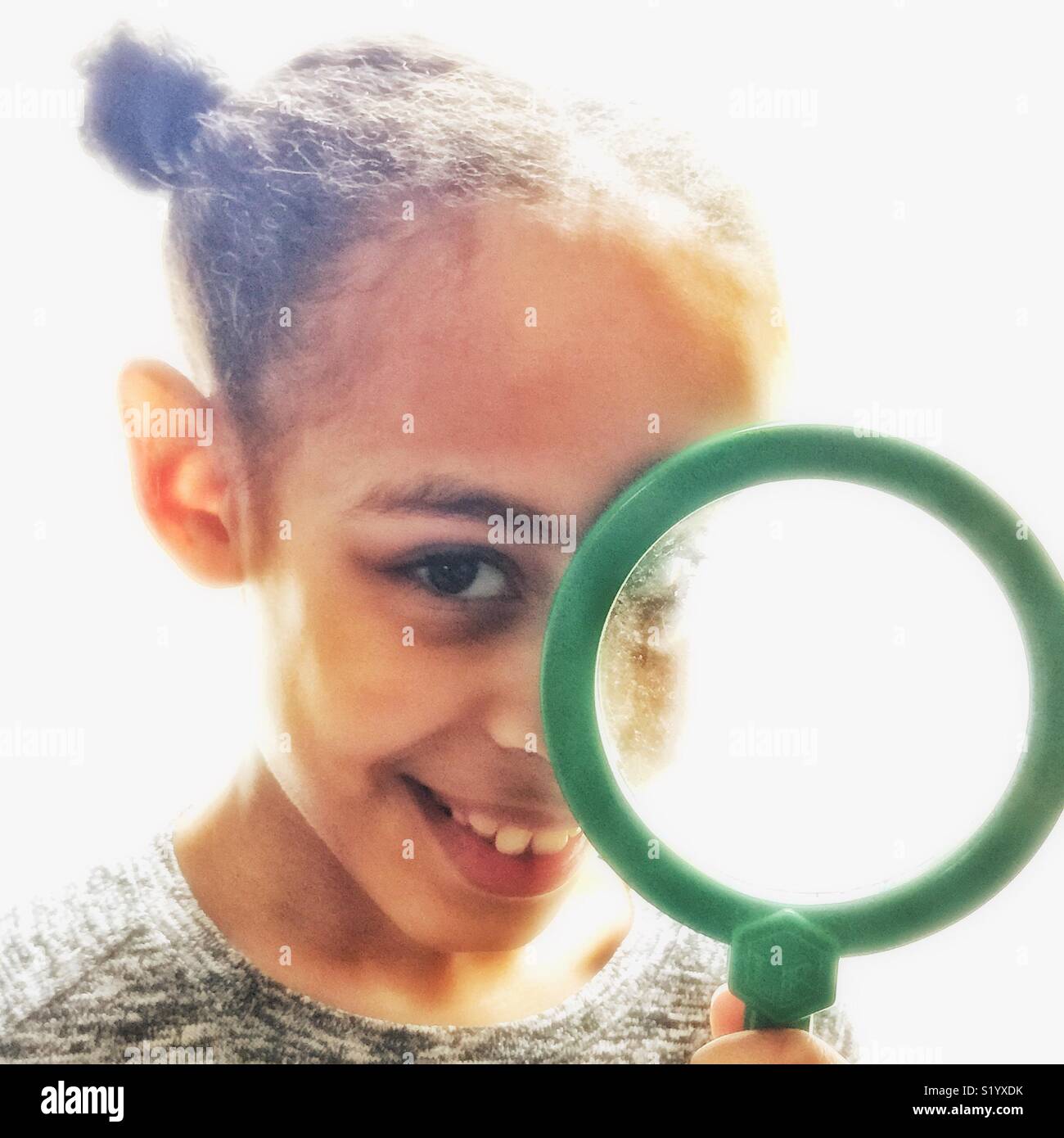 A young girl looks through a magnifying glass. Stock Photo
