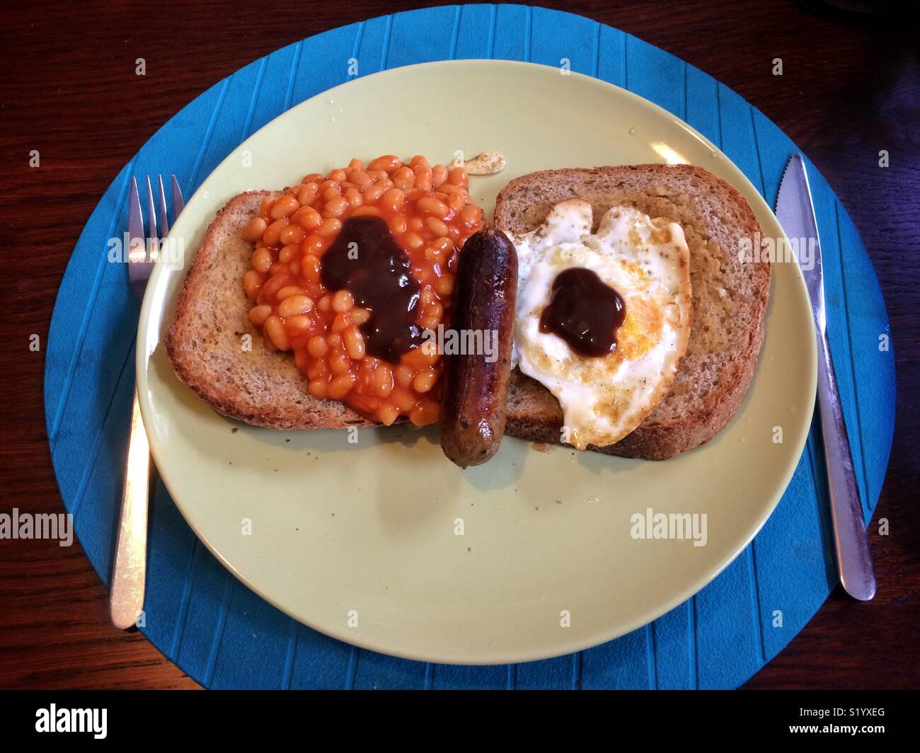 A veggie breakfast with toast, fried egg, beans and a vegetarian sausage and brown sauce. It looks like a face! Stock Photo