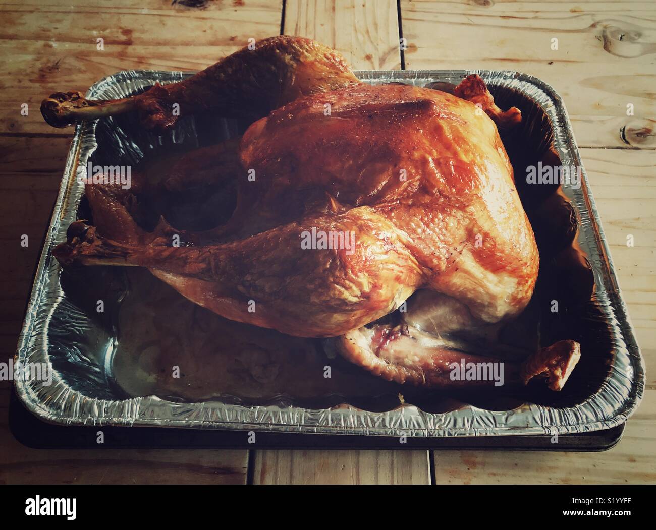 Golden brown, just roasted turkey in an aluminum pan on a rustic wooden table Stock Photo