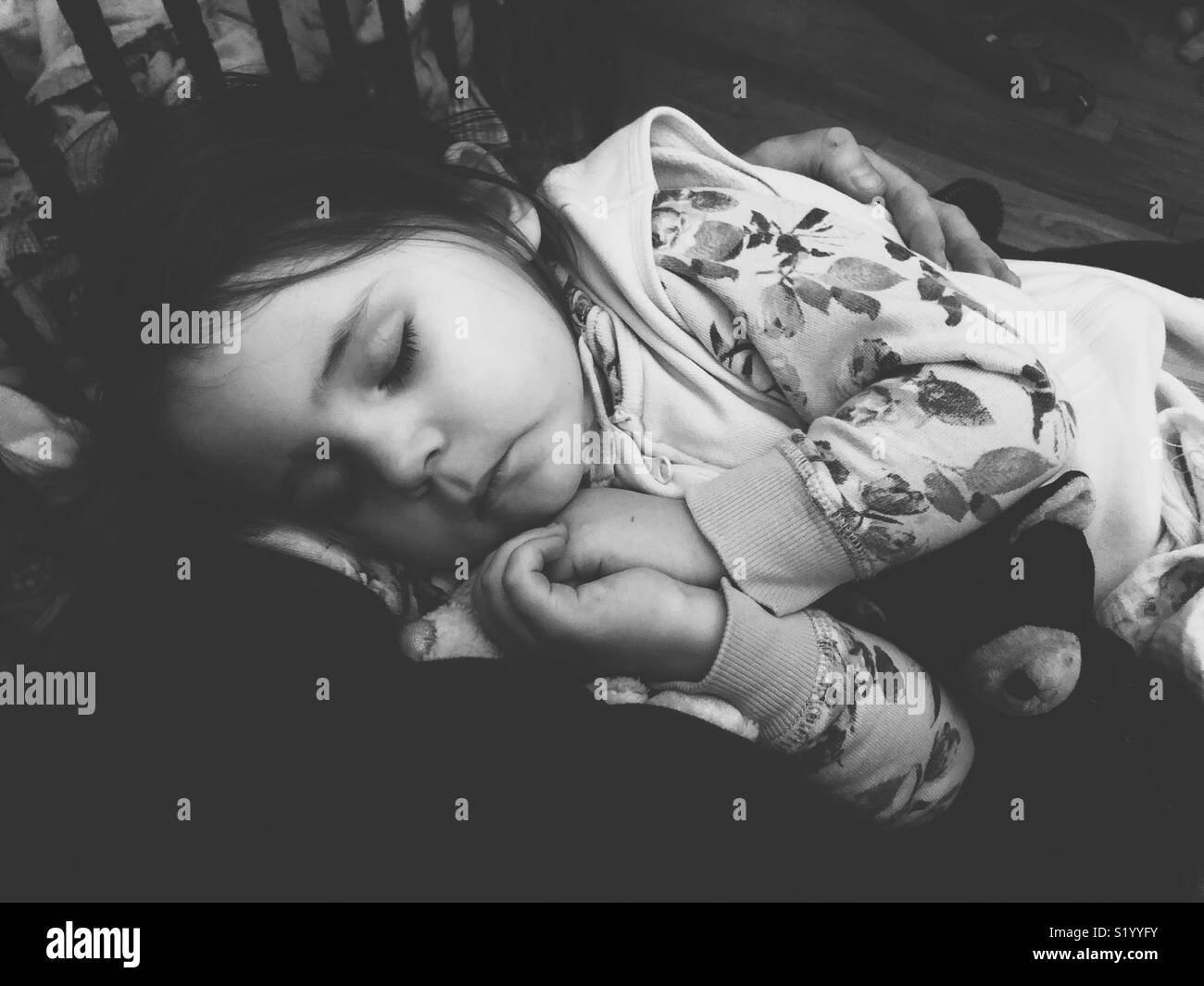 Black and white image of sleeping toddler in mother’s arms from mother’s perspective with crib bars in background - Smartphone Captured Stock Image