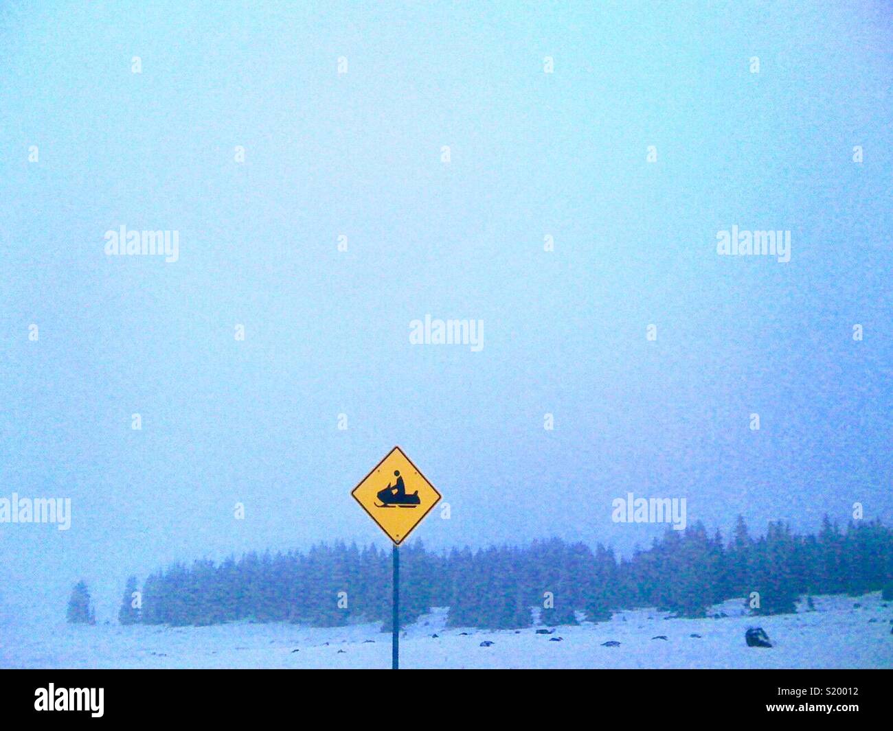 Snowmobile crossing sign in a winter snowy evergreen forest. - Smartphone Captured Stock Image