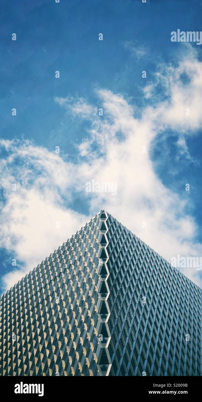 An tall, thin image of a pointed building with a diamond patterned architecture against a blue sky with clouds - Smartphone Captured Stock Image