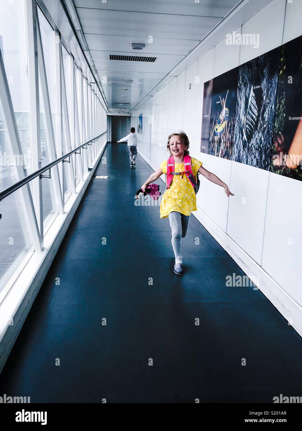 Two children pretend to be airplanes in an airport gangway. - Smartphone Captured Stock Image