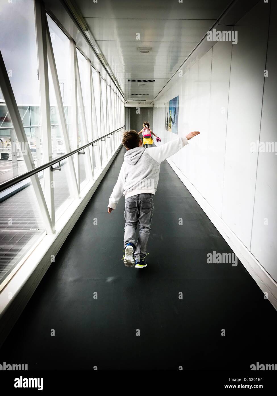 Two children pretend to be airplanes in an airport gangway. - Smartphone Captured Stock Image
