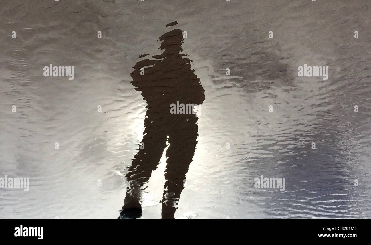 Reflection of person in water on beach Stock Photo