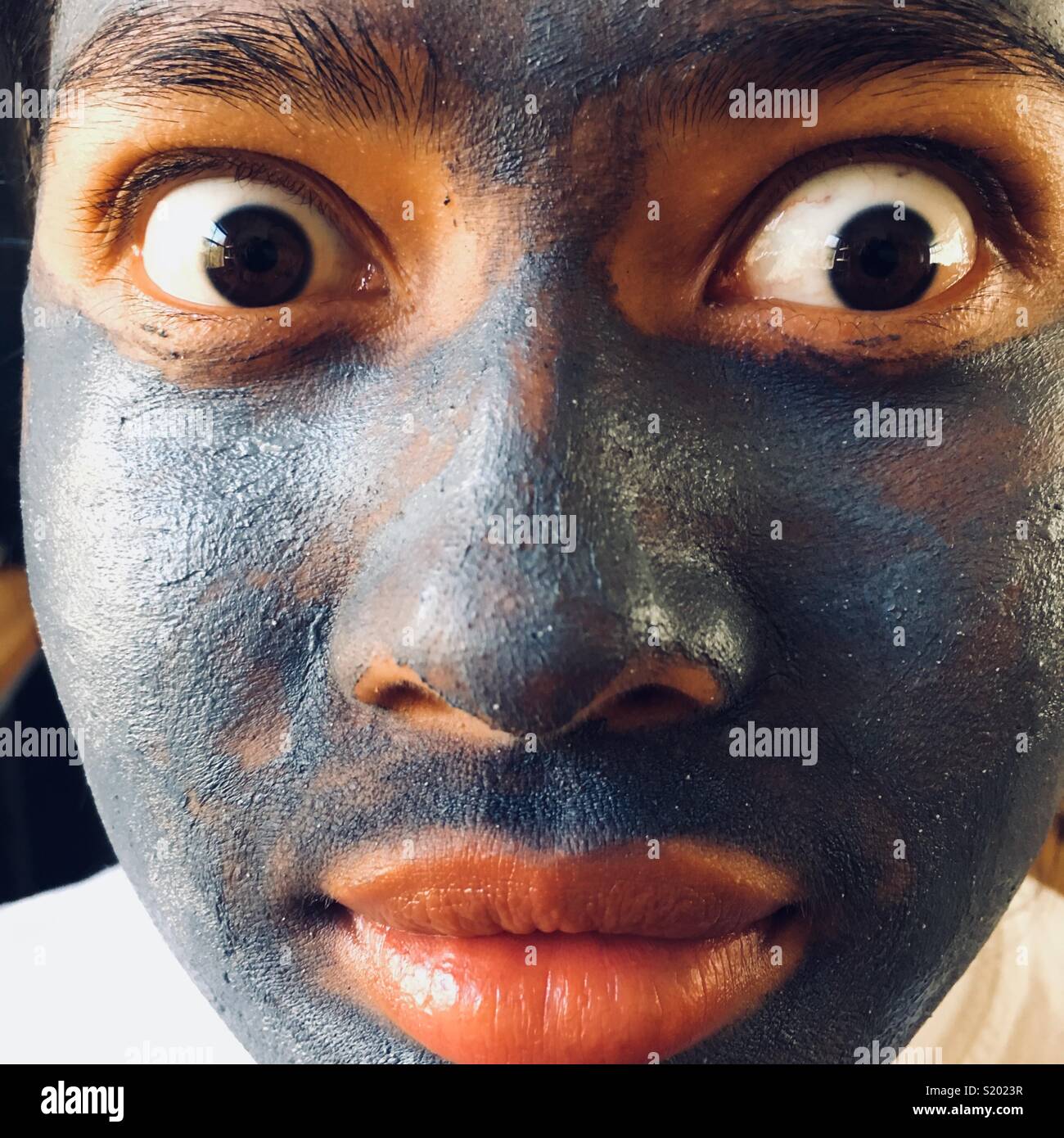 Girl with surprised eyes in blue mud pack face mask Stock Photo
