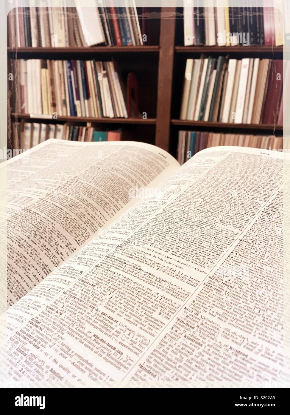 An open large dictionary in front of a bookcase filled with hardback books, United States. - Smartphone Captured Stock Image