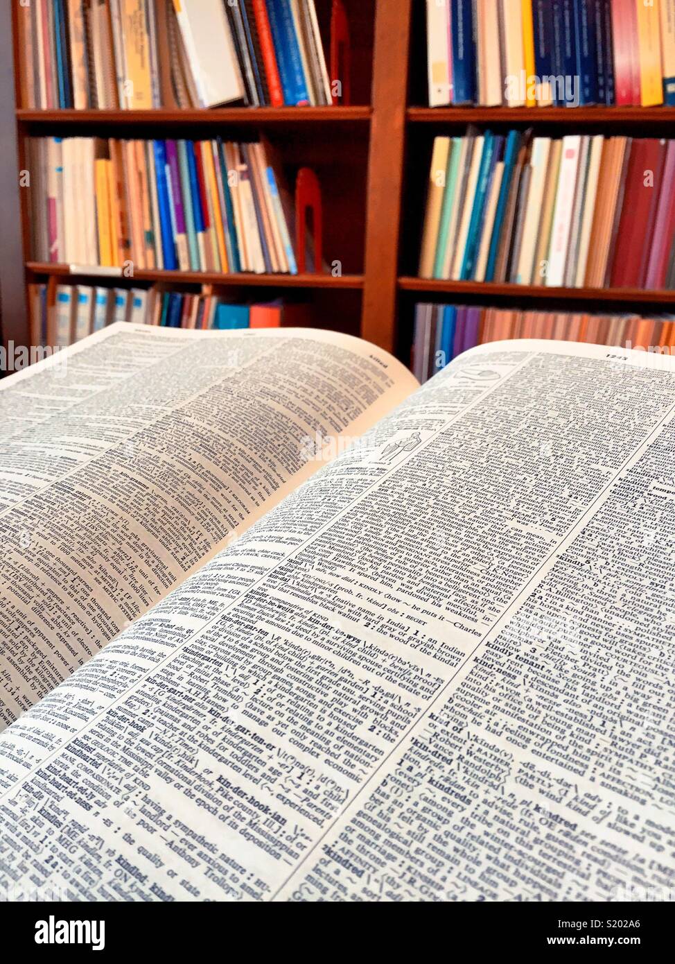 Open large dictionary in front of a book case filled With books, USA - Smartphone Captured Stock Image
