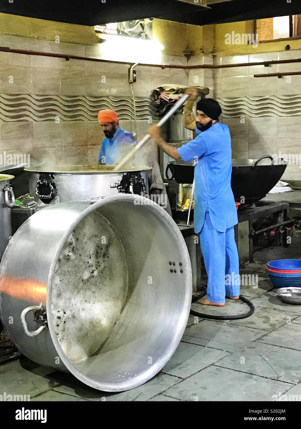 Workers in a mosque’s kitchen prepare meals in massive pots. - Smartphone Captured Stock Image