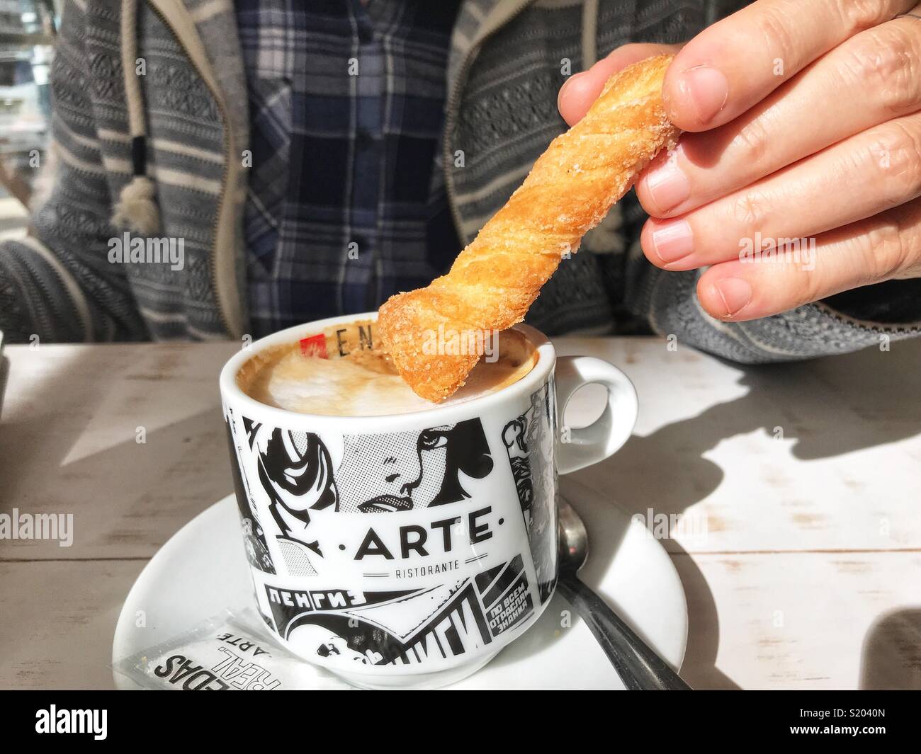 Woman dunking a biscuit into a cup of cappuccino coffee in a cafe, midsection view - Smartphone Captured Stock Image