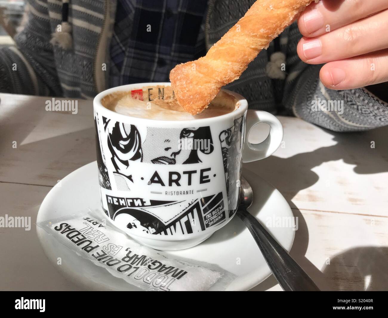 Woman dunking a biscuit into a cup of cappuccino coffee in a cafe, midsection view - Smartphone Captured Stock Image