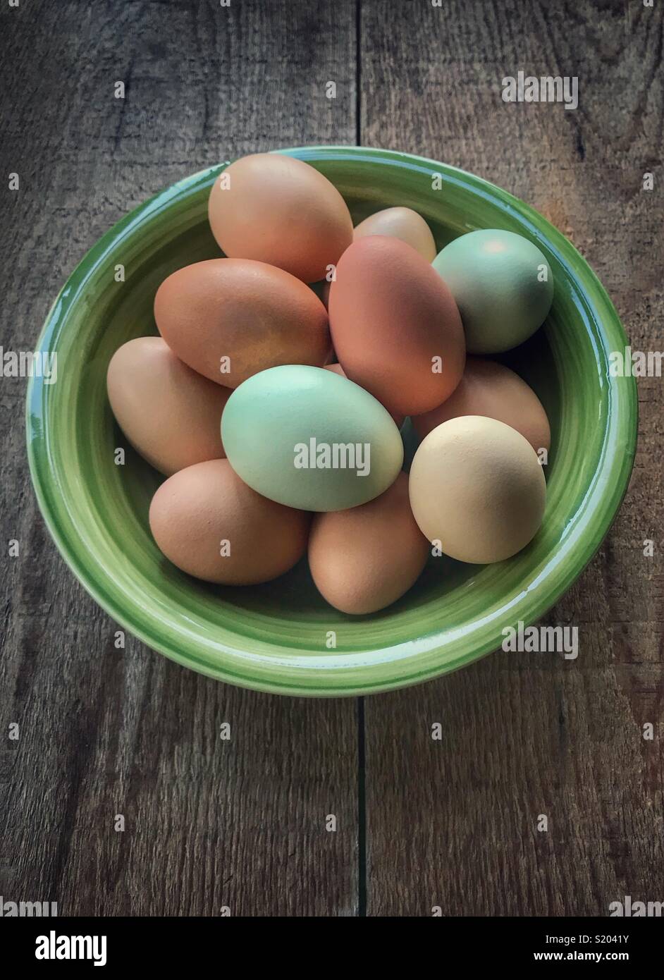Freshly collected colorful backyard chicken eggs in in green bowl on a wood table - Smartphone Captured Stock Image